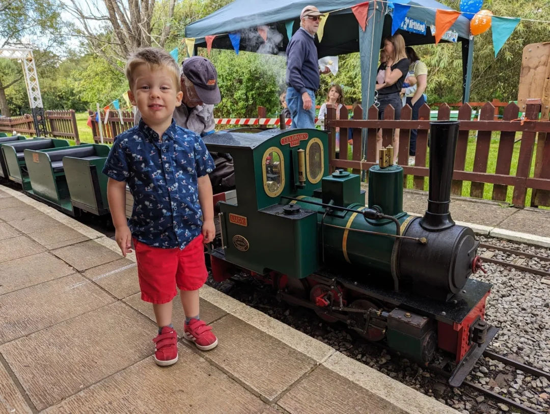 A child beside the miniature green train in the Bridge House garden